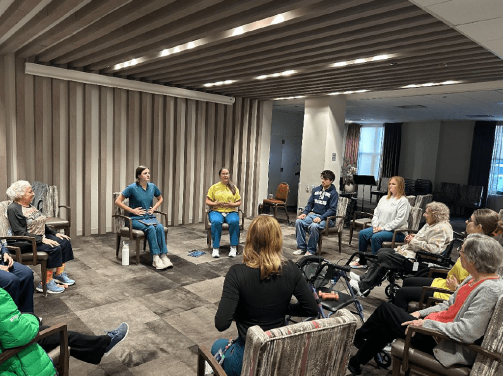 Das Bild zeigt Karlo in einem Stuhlkreis sitzend, gemeinsam mit jüdischen Seniorinnen.